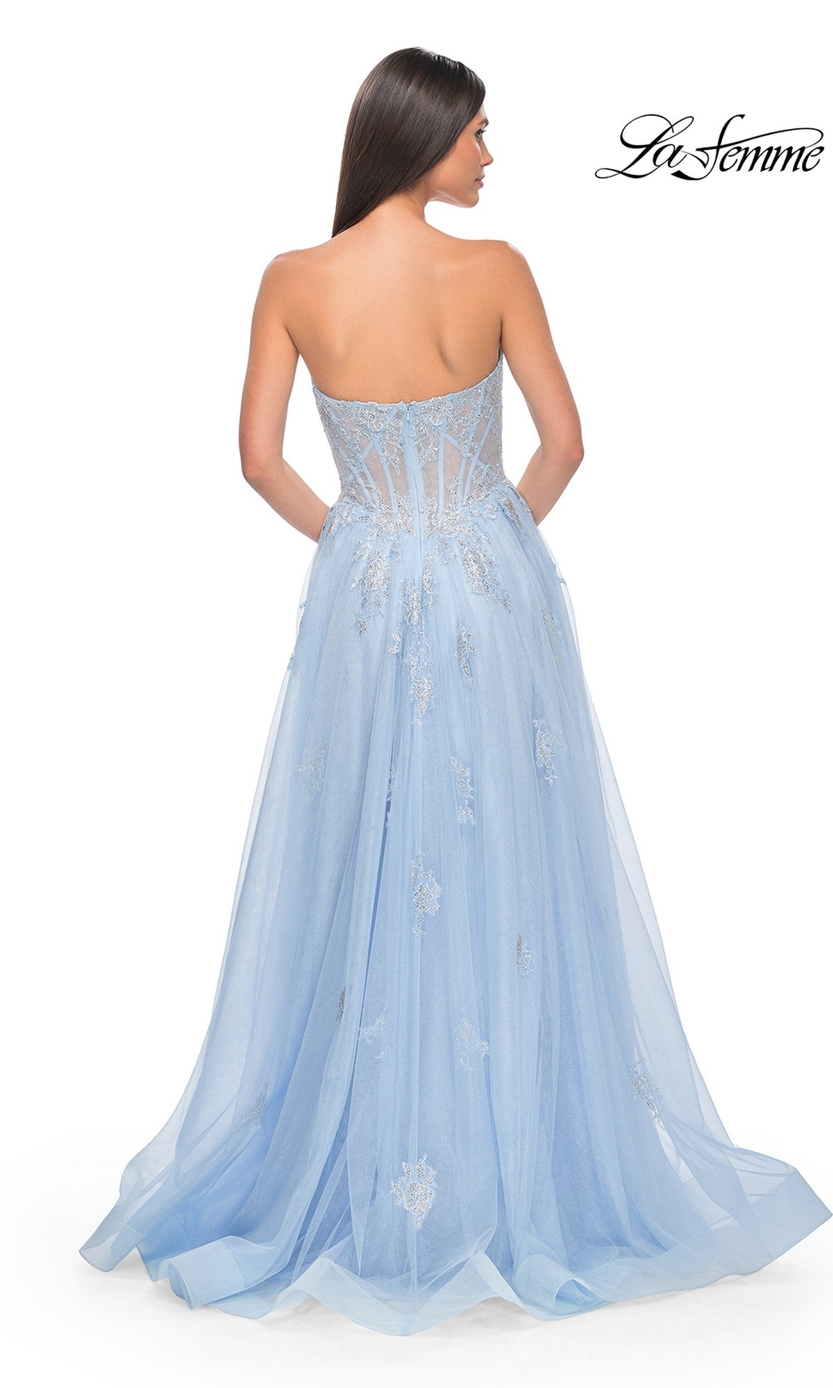 A woman with long brown hair is shown from the back, wearing the La Femme Strapless Long A-Line Prom Dress 32111 in light blue, featuring a sheer embellished bodice with embroidered-lace appliques and a flowing tulle skirt.